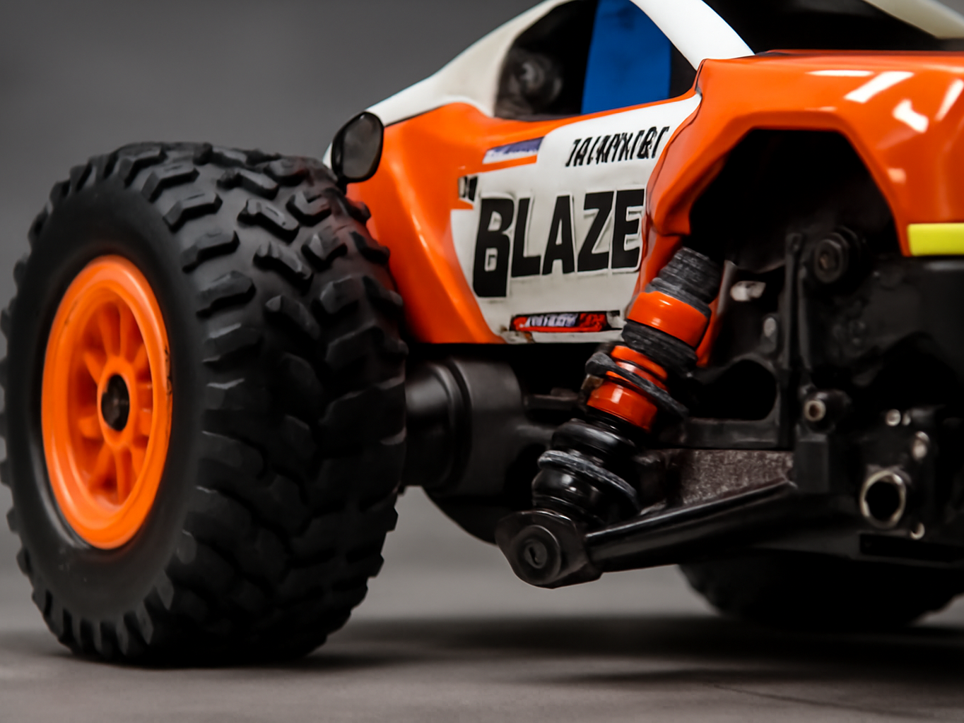 Macro close-up of DEERC 1205 RC truck's front suspension and grip tires with shallow depth of field